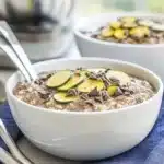 Creamy chocolate zucchini overnight oats in a glass jar topped with shredded coconut and dark chocolate shavings.