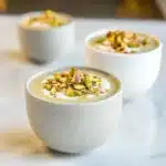 Glass jar filled with creamy pistachio overnight oats topped with crushed pistachios and a drizzle of honey on a light background.