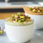 Close-up of pistachio overnight oats layered in a glass, topped with chopped pistachios and served on a neutral background.