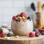 Glass jar filled with oat bran overnight oats topped with almond butter, banana slices, and hemp seeds on a wooden table.