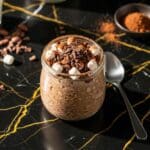 Hot cocoa overnight oats in glass jar topped with chocolate shavings and marshmallows on black marble counter